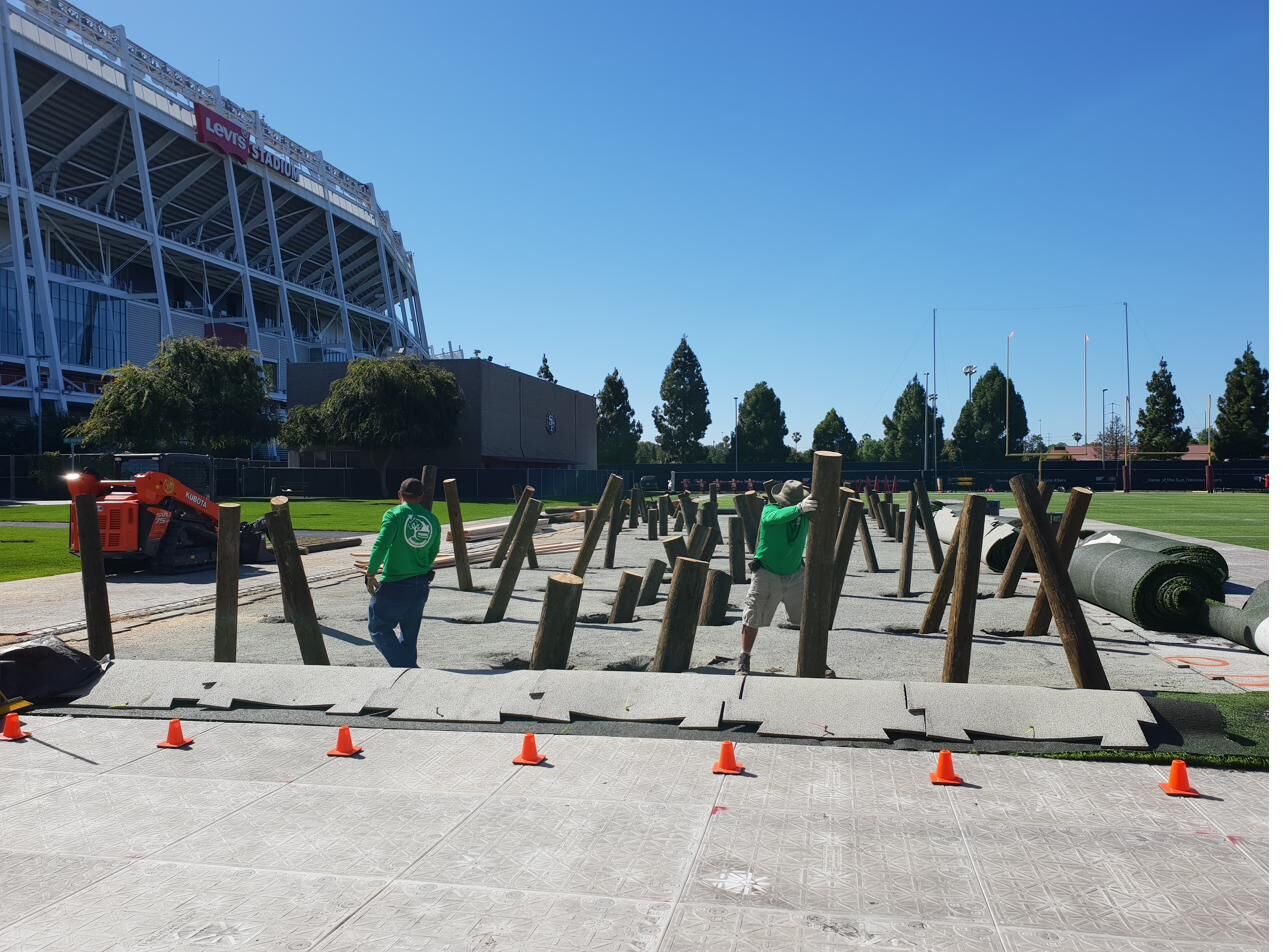 Green Constructors crew in branded shirts installing wooden posts on the 49ers practice field