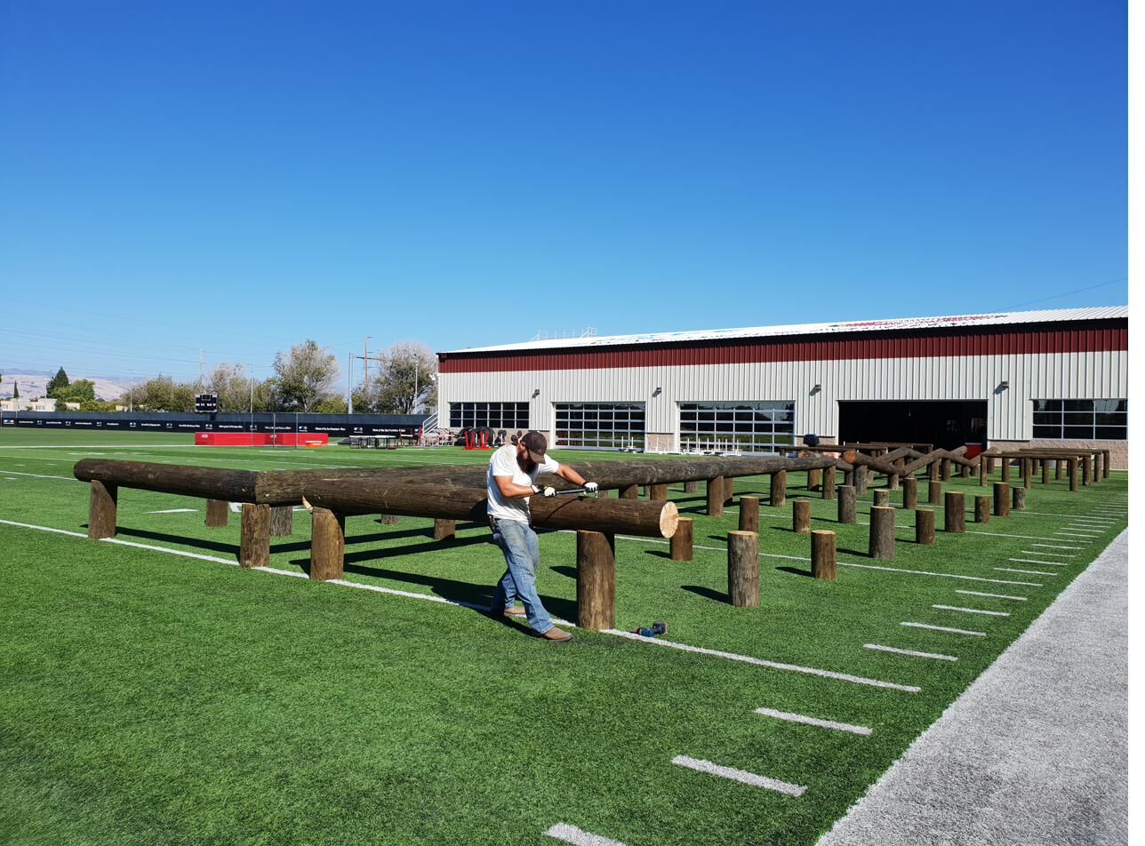 Crew measuring a long log beam to length with the 49ers field house in the background