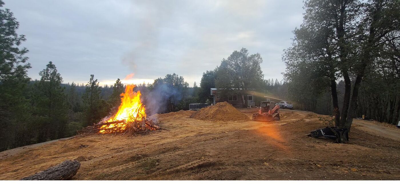 Controlled brush pile burn at dusk with equipment on site