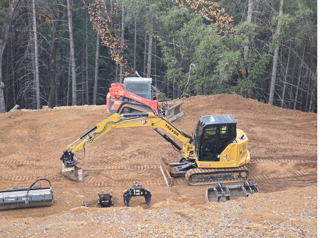 Green Constructors equipment fleet — Kubota SVL 75-2 skid steer and CAT 306 excavator with attachments on a freshly graded forest pad