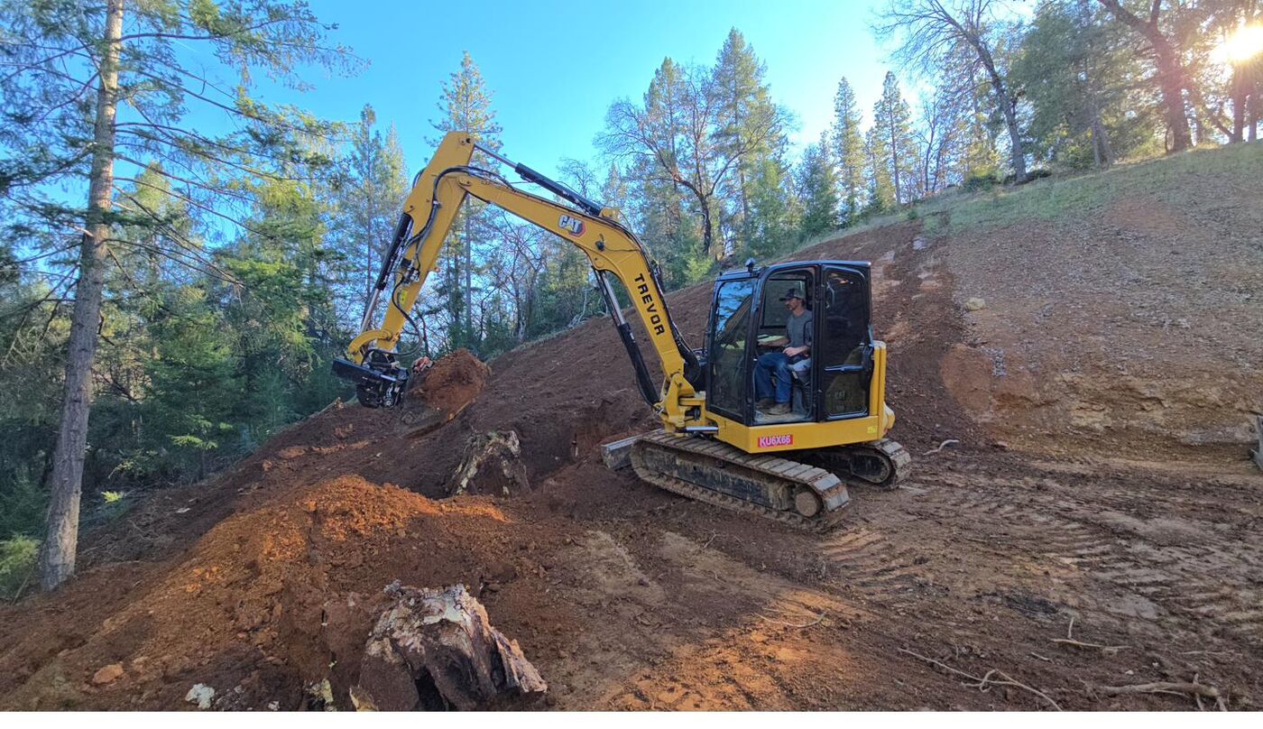 CAT 306 excavator cutting a forest hillside during road construction